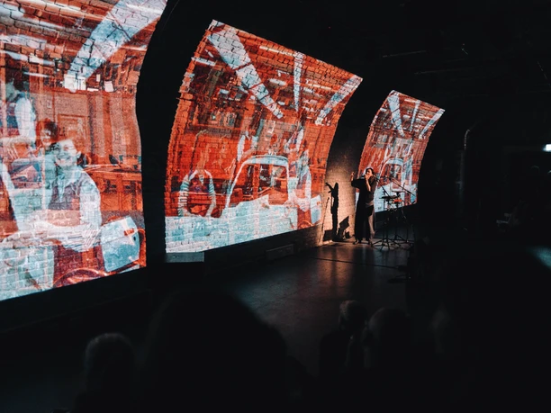 Yoldaş – Frauen, die einander halten Künstler vor leuchtenden Projektionen in gemauertem Tunnelraum während einer Performance
