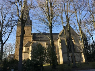 Eselsweg Steinerne Kirche mit Turm in Isselhorst, umgeben von kahlen Bäumen unter blauem Himmel