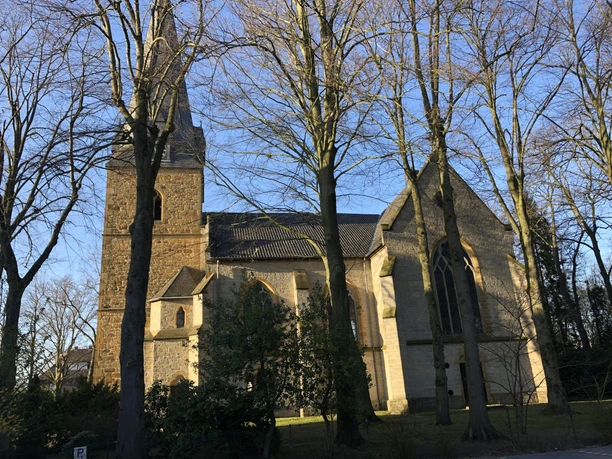 Eselsweg Steinerne Kirche mit Turm in Isselhorst, umgeben von kahlen Bäumen unter blauem Himmel