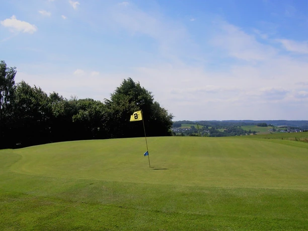 Golfanlage Gimborner Land Weite Golfbahn mit Flagge vor Baumkante und Blick auf sanfte Hügel im Hintergrund