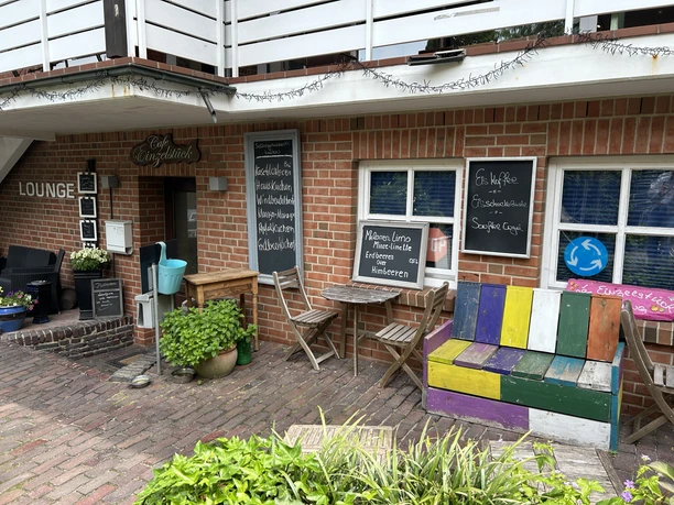 Außenbereich des Café Einzelstück Außenbereich des Café Einzelstück mit einer bunten Holzbank, Tischen und beschriebenen Kreidetafeln.
