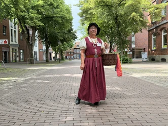 Lucia Voigtländern Gästeführerin in historischer Kleidung mit Korb auf einem gepflasterten Platz in Nienburg.