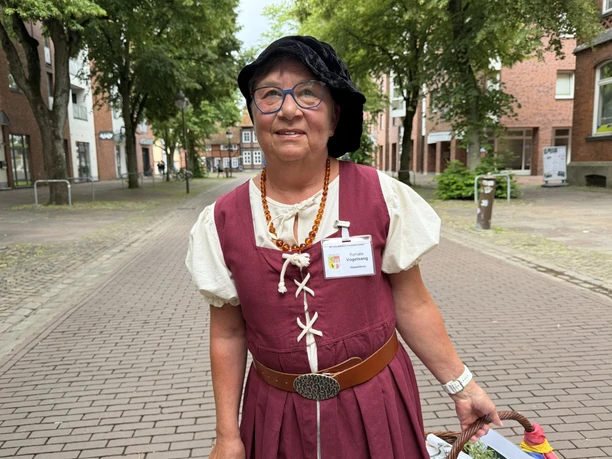 Lucia Voigtländern Gästeführerin in weinroter historischer Tracht steht auf einer gepflasterten Straße.