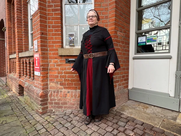 A tour guide in historical costume is standing in front of the brick building that houses the tourist information office.
