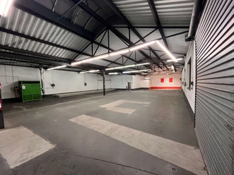 Leere Industriehalle mit Betonboden, Metallträgern und hellen LED-Linien an der Decke