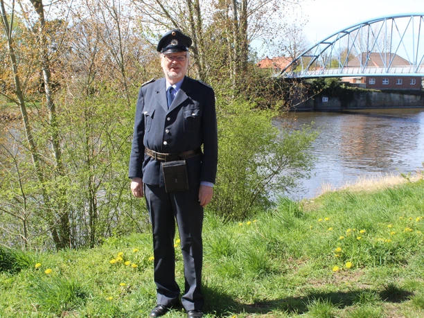 A tour guide in historical uniform is standing on the banks of the Weser in Nienburg.