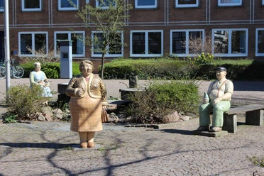 Lechner Figuren Die bunten Lechner-Skulpturen Frau Peters, Herr Hagen und Mathilde auf einem gepflasterten Platz.