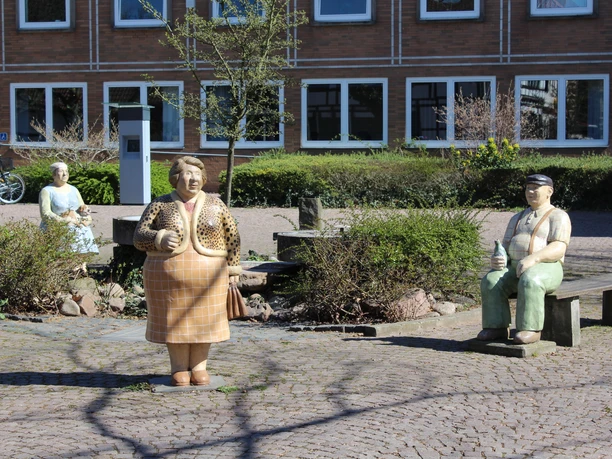 Lechner Figuren Die bunten Lechner-Skulpturen Frau Peters, Herr Hagen und Mathilde auf einem gepflasterten Platz.