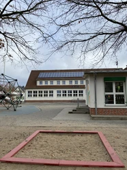 Außenansicht der Grundschule Ehmen-Mörse mit Schulhof, Sandkasten und einem Klettergerüst.