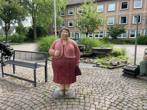 Frau Peters Die farbenfrohe Lechner-Figur "Frau Peters" steht mit rosa Jacke auf dem Platz in Petershagen.