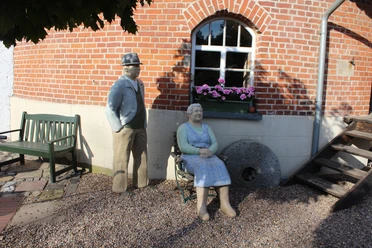 Lebensgroße Figuren des Müllerpaars Karl und Liesel Meyer vor einer Backsteinwand mit Mühlstein.