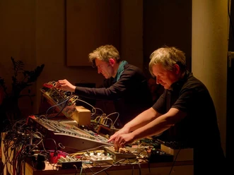 Soundings #055: Gebrüder Teichmann Zwei Personen arbeiten an elektronischen Klanggeräten in warm beleuchtetem Raum.
