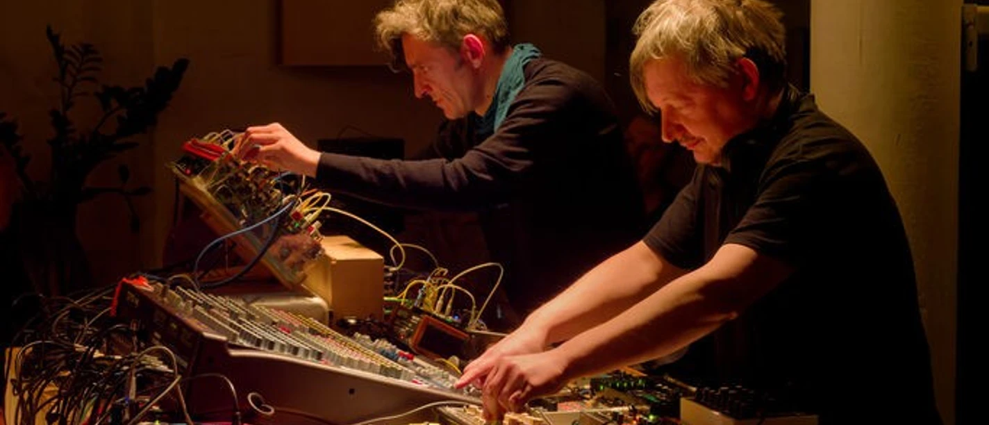 Soundings #055: The Teichmann Brothers Two people are working on electronic sound equipment in a warmly lit room.