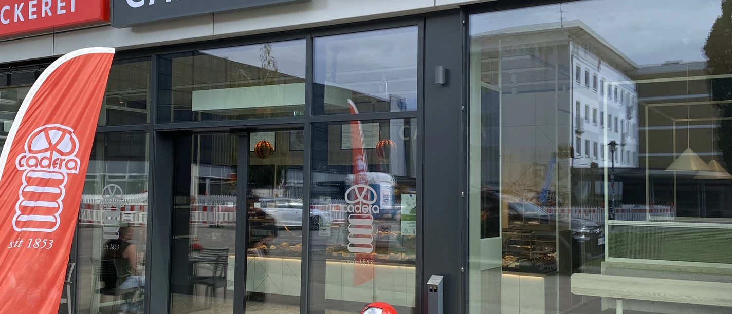 Die Außenfassade der Bäckerei Konditorei Cadera mit moderner Glasfront und roter Beschriftung.