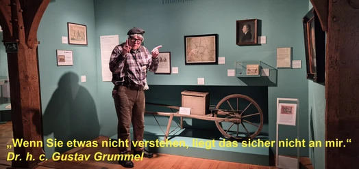 Museumsraum mit Gustav Grummel zwischen historischen Exponaten und gelbem Zitat.