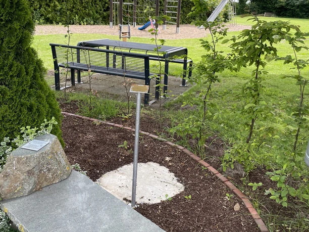 Heinrich Nagel mit Steinbank und Tafel. Im Hintergrund ein Spielplatz umgeben von Grün.