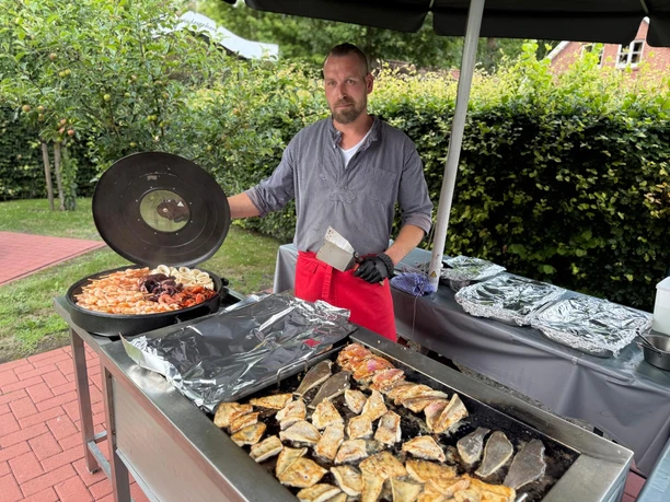 Fischauswahl Grillbuffet Hengstforder Mühle.jpeg Ein Koch bereitet bei einem Grillbuffet im Freien Fisch und Meeresfrüchte zu.
