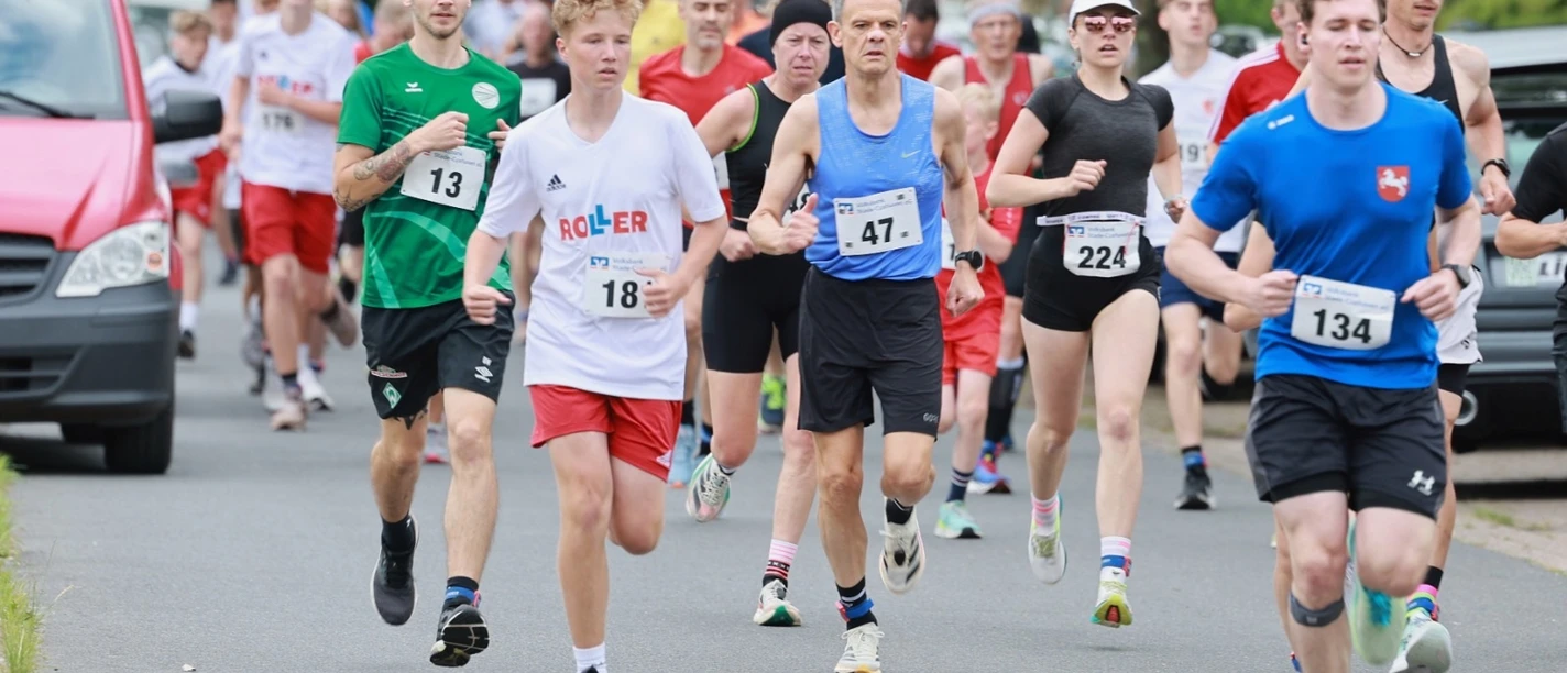 Brückenlauf.jpg Sportliche Läuferinnen und Läufer voller Energie bei einem Wettkampf auf einer Allee.