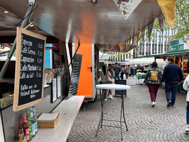MarktTreff at Rudolfplatz Coffee stand with a price board at the MarktTreff on Rudolfplatz under green trees