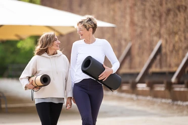 Zwei Frauen gehen lächelnd mit Yogamatten durch den Kurpark Bad Salzuflen