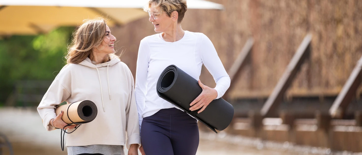Zwei Frauen gehen lächelnd mit Yogamatten durch den Kurpark Bad Salzuflen