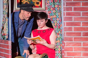 Hafen Revue Theater Theaterszene: Ein Seemann schaut einer lesenden Frau in rotem Kleid über die Schulter.