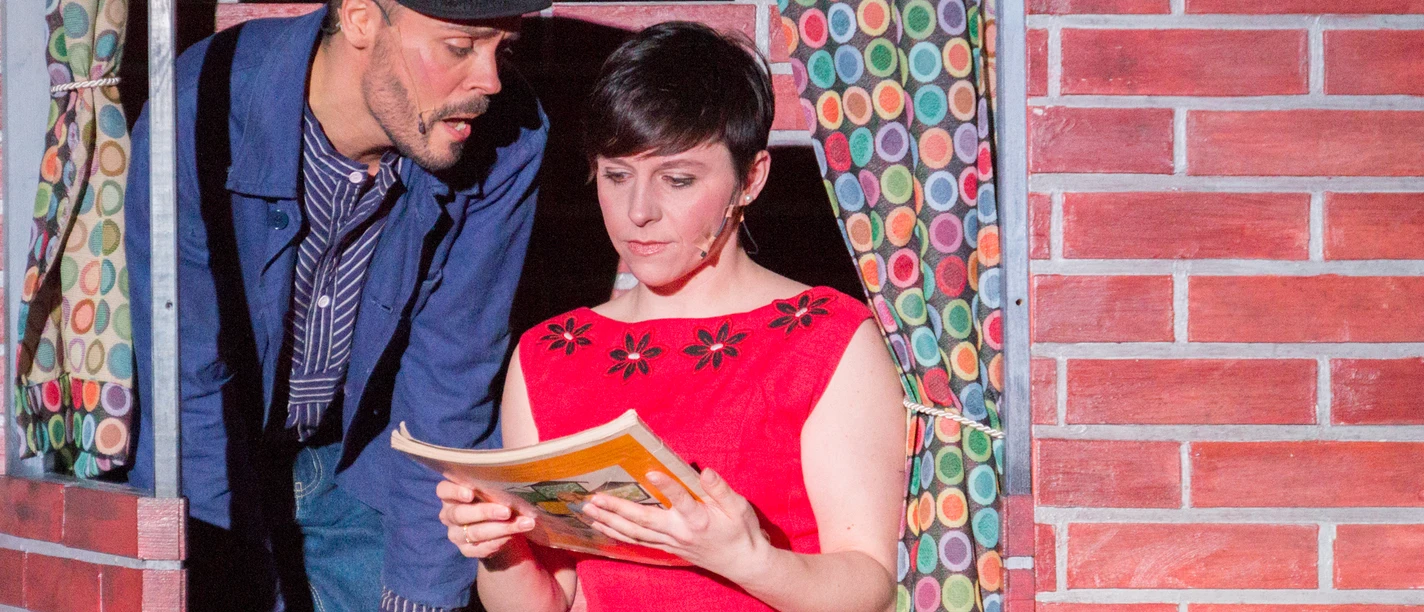 Hafen Revue Theater Theaterszene: Ein Seemann schaut einer lesenden Frau in rotem Kleid über die Schulter.