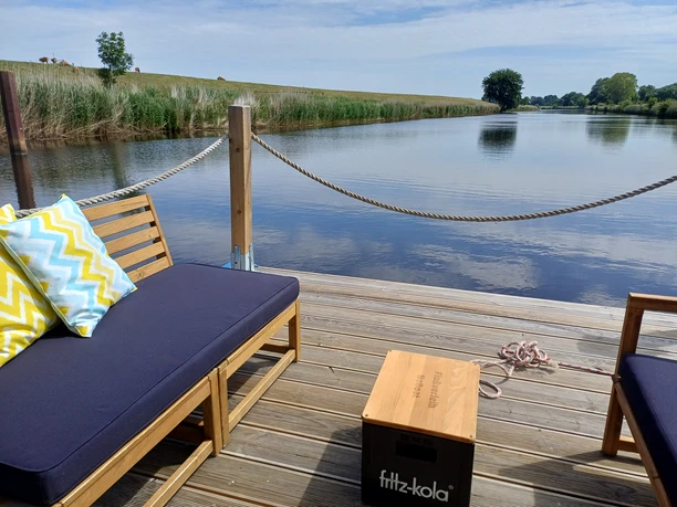 Ein Sonnendeck auf einem Floß am Kanal lädt zum Verweilen mit Blick ins Grüne ein.