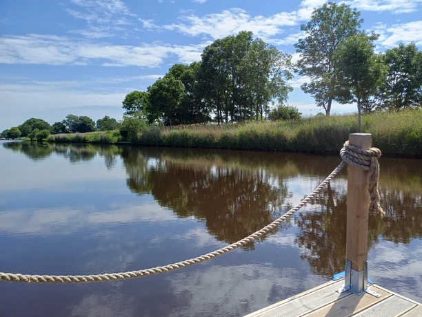 NoBoatGermany Nordseebad Otterndorf Ausblick vom Floß auf dem Hadelner Kanal in Otterndorf. Das grüne Ufer spiegelt sich im ruhigen Wasser.