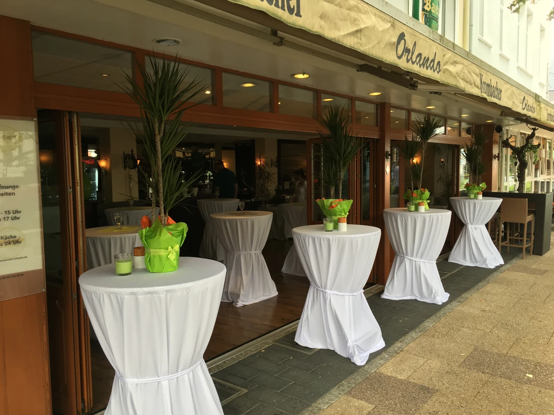 Terrasse Auf dem Bild ist die Terrasse des Restaurants zu sehen, ausgestattet mit elegant weiß eingedeckten Stehtischen. Die Atmosphäre ist einladend und perfekt für ein entspanntes Essen im Freien.