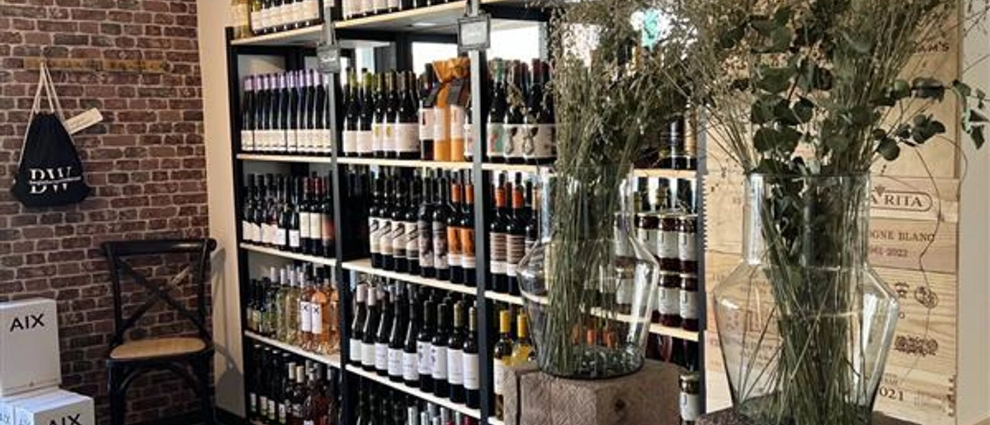 Weinhandel Kork & Kante Weinregale in einer Weinhandlung mit Holzkistenwand und großen Glasvasen im Vordergrund