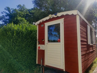 Übernachten im Bauwagen auf dem Hasthaushof in Ratingen Ein roter Bauwagen als Übernachtungsmöglichkeit auf dem Hasthaushof in Ratingen, umgeben von Hecke und Bäumen.