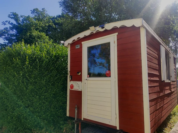 Übernachten im Bauwagen auf dem Hasthaushof in Ratingen Ein roter Bauwagen als Übernachtungsmöglichkeit auf dem Hasthaushof in Ratingen, umgeben von Hecke und Bäumen.