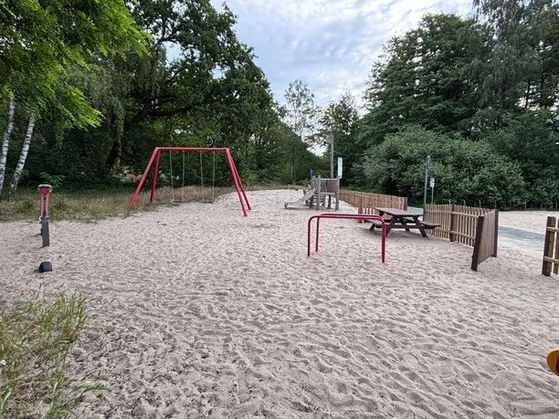 Spielplatz Weiße Düne Spielplatz an der Weißen Düne mit einer Schaukel, einer Rutsche und einer Wippe. und im Hintergrund ist das Steinhuder Meer zu sehen. Als Abgrenzung sind einige halbhohe Holzzäune in dem Bereich.