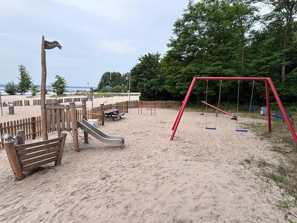 Spielplatz Weiße Düne Spielplatz an der Weißen Düne mit einer Schaukel, einer Rutsche und einer Wippe. und im Hintergrund ist das Steinhuder Meer zu sehen. Als Abgrenzung sind einige halbhohe Holzzäune in dem Bereich.
