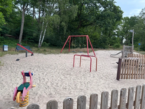Spielplatz Weiße Düne (4).jpg Spielplatz an der Weißen Düne mit einer Schaukel, einer Rutsche und einer Wippe. und im Hintergrund ist das Steinhuder Meer zu sehen. Als Abgrenzung sind einige halbhohe Holzzäune in dem Bereich.