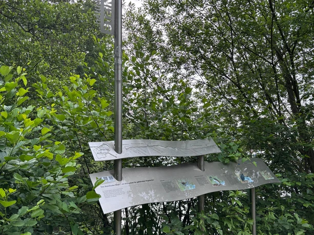 Infostele Alte Moorhütte Eine silberne Infotafel mit Informationen zum Naturpark vor einem Gebüsch. Links an der Seite ist ein 3D-Schriftzug "Steinhuder Meer" angebaut.