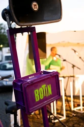 BOTIN A purple BOTIN box with a speaker in front of a blurred stage and microphones.