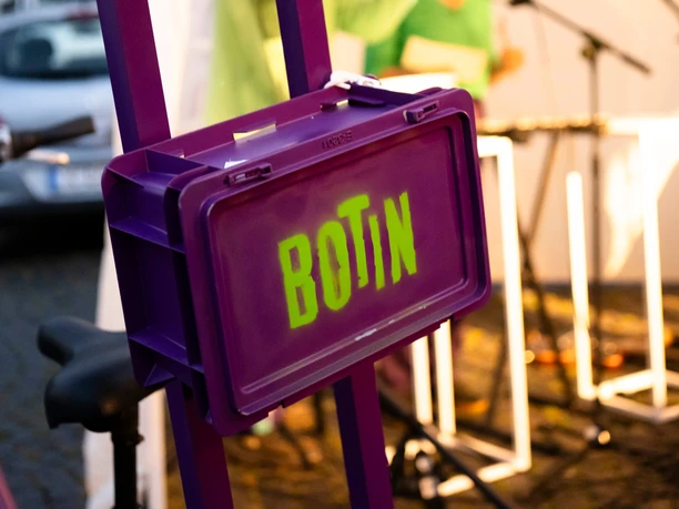 BOTIN A purple BOTIN box with a speaker in front of a blurred stage and microphones.