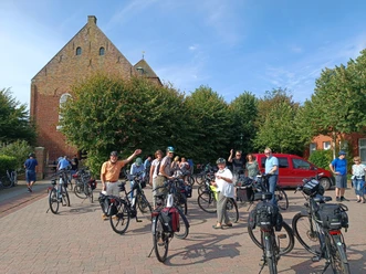 Krummhörner Kirchturm-Tour: Uttum Eine Gruppe Radfahrer pausiert während der Krummhörner Kirchturm-Tour vor der Kirche in Uttum.