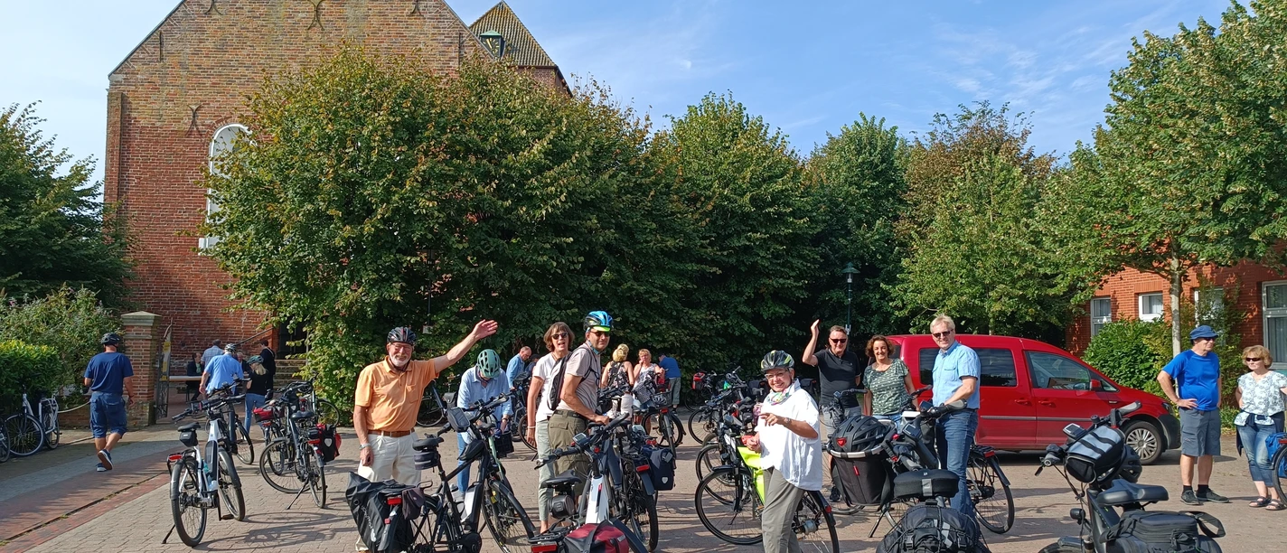 Krummhörner Kirchturm-Tour: Uttum Eine Gruppe Radfahrer pausiert während der Krummhörner Kirchturm-Tour vor der Kirche in Uttum.