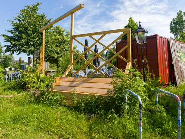 Beet T0469 (c) Helmut Gross_Erlebnis Bremerhaven_WEB.jpg Außenansicht vom Café Das Beet: eine Holz-Sitzecke im Garten neben einem roten Container.