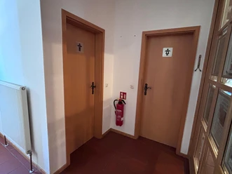 Toilette Haus des Gastes - innen Zwei Türen nebeneinander die zu den Toiletten führen. Zwischen den Türen hängt ein Feuerlöscher.
