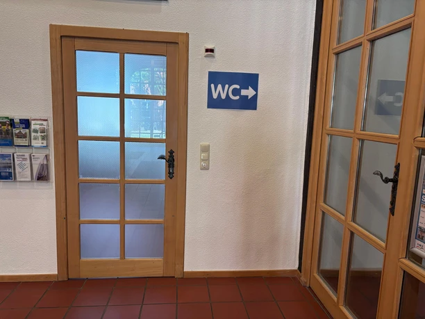 Toilette Haus des Gastes - innen Eine Tür links und eine Tür rechts. Beide Türen haben Holzrahmen und Glasscheiben. Zwischen den Türen ist ein Schild mit der Aufschrift "WC".