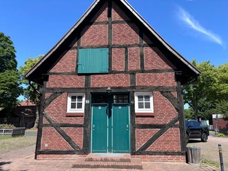 Toilette Aloys-Bunge-Platz (2) Blick auf ein altes Fachwerkhaus mit grüner Tür und jeweils einem kleinen Fenster daneben. Oben am Haus ist eine grüne Fensteröffnung.