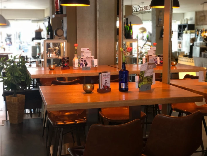 Barzzano Nienburg Modernes Café mit hölzernen Tischen, Ledersesseln und dekorativen Details in warmem Licht.