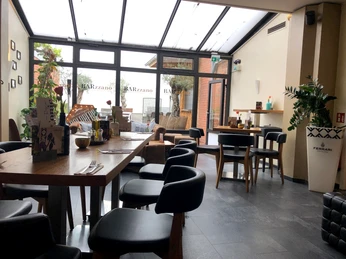 Barzzano Nienburg Ein helles Restaurant mit modernem Interieur, Holztischen und schwarzen Stühlen in einem Wintergarten.