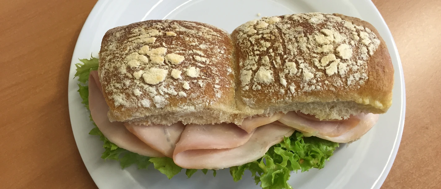 belegtes Brötchen Frisches Brötchen mit Salatblatt und saftigem Schinken auf einem weißen Teller angerichtet.