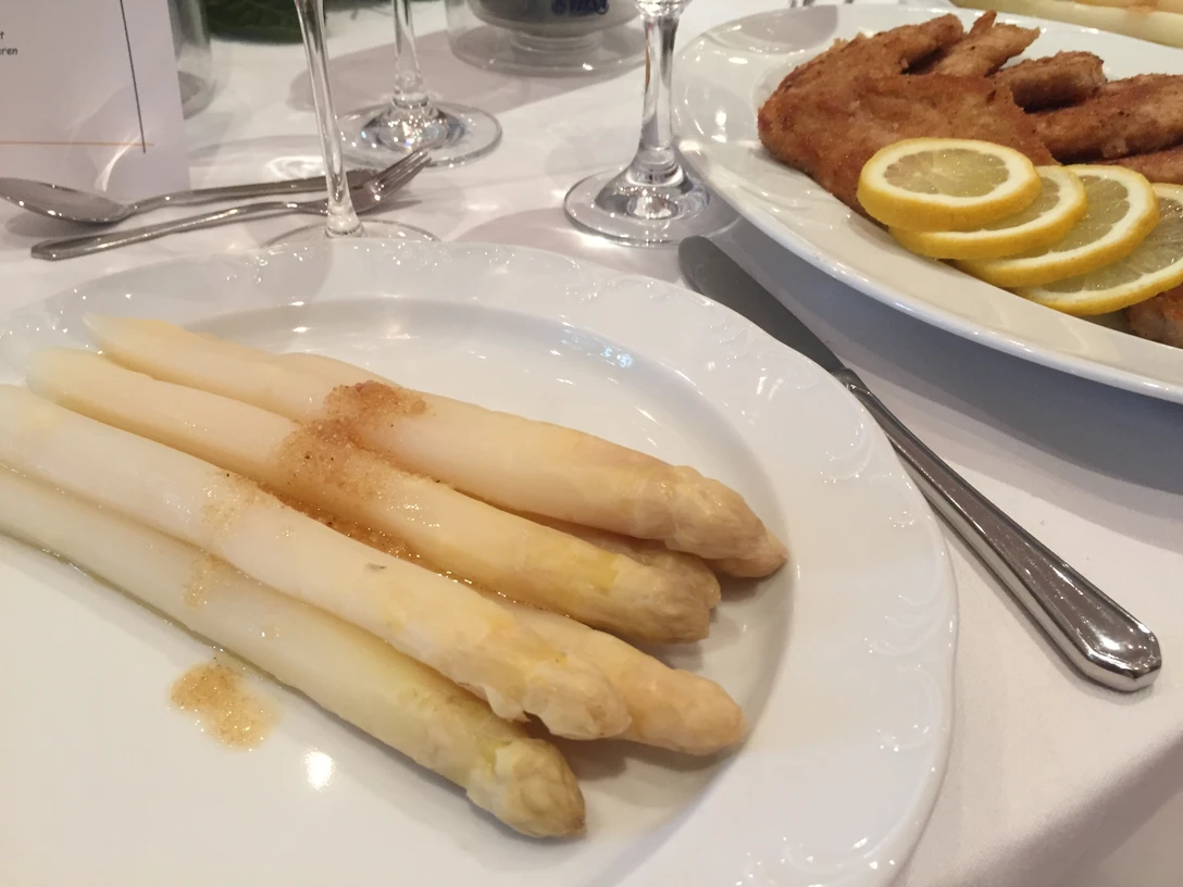 Ein Teller mit weißem Spargel, serviert mit Sauce, neben einem Wiener Schnitzel mit Zitronenscheiben.
