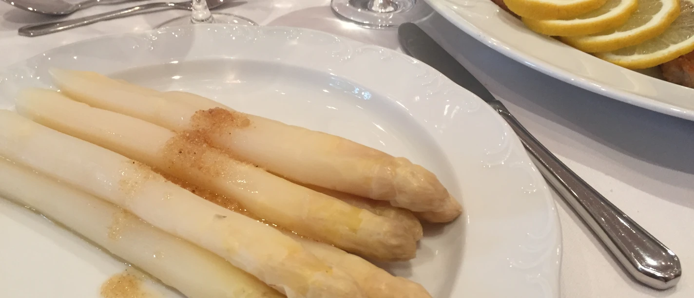 Spargelgericht Ein Teller mit weißem Spargel, serviert mit Sauce, neben einem Wiener Schnitzel mit Zitronenscheiben.